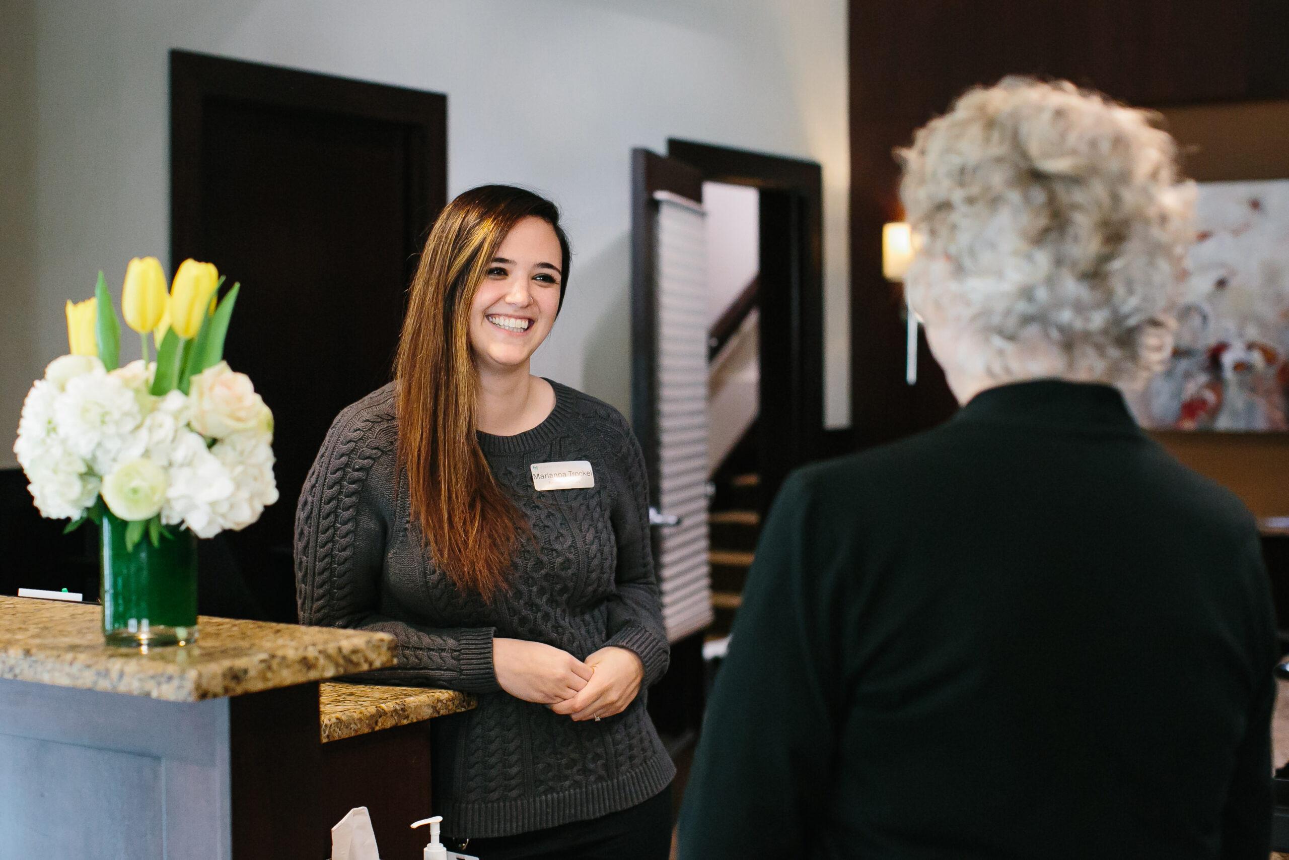 A front desk employee smiles and talks to someone who is facing away from the camera.