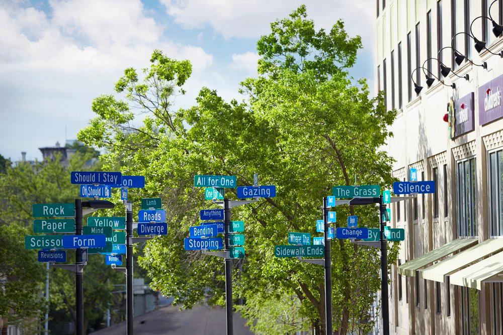 An art display of street signs labeled with playful words such as Rock, Paper, Scissors.