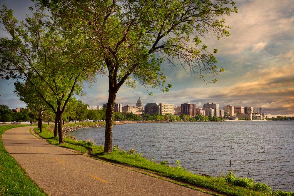 A picturesque walking trail next to a lake. The Capitol Lakes skyline can be seen in the distance.