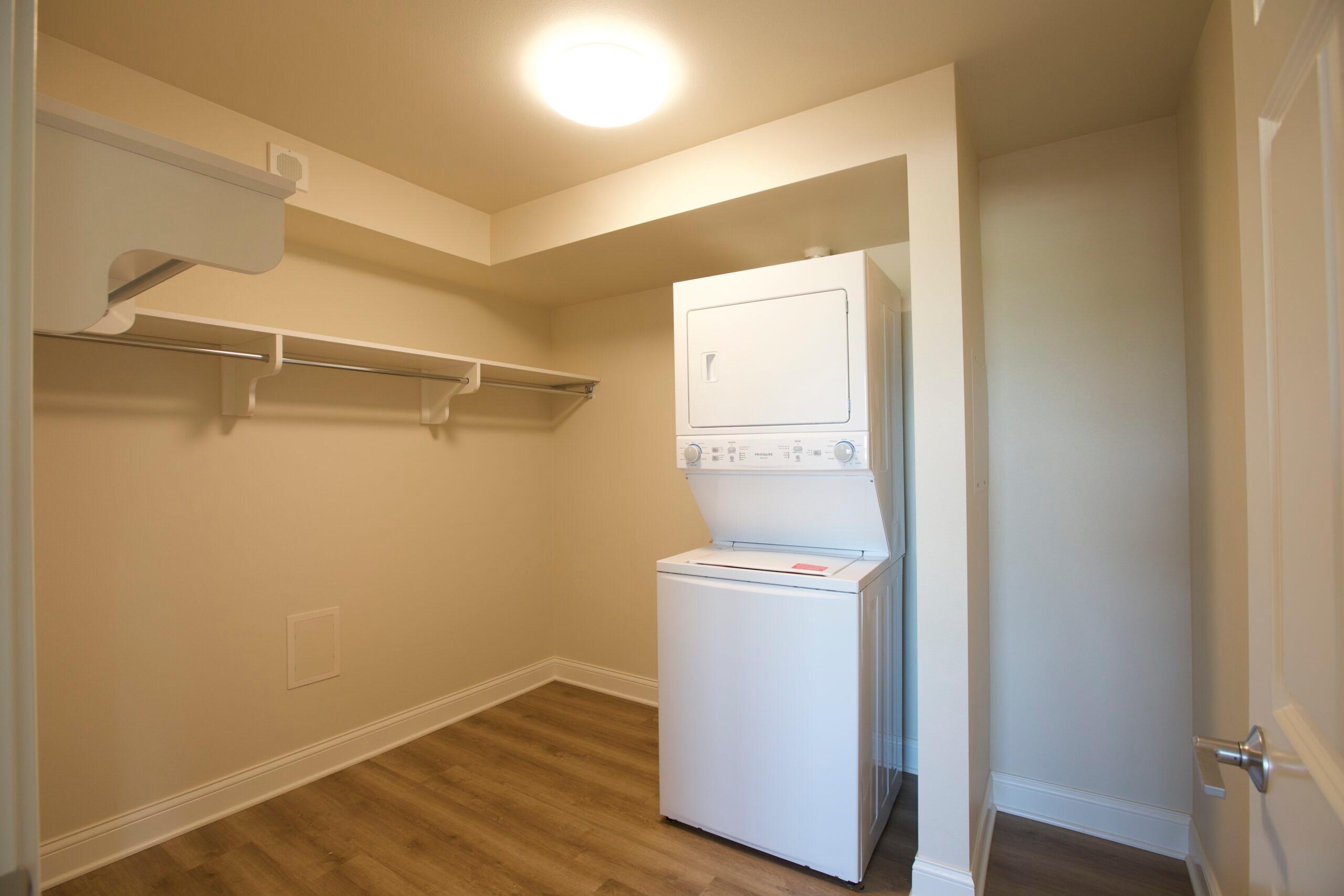 A closet with a washer and dryer and space to hang clothes.