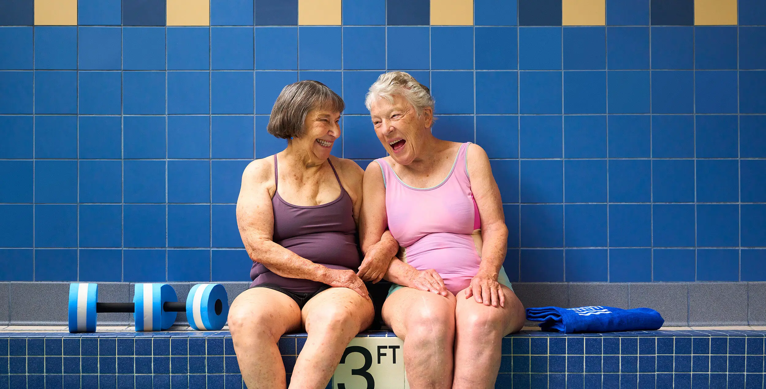 Capitol Lakes residents Joan and Nancy sitting next to each other on the edge of the pool, smiling and laughing.